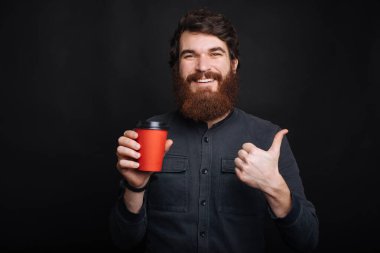 Gülümseyen sakallı hippi elinde bir fincan kahveyle baş parmağını kaldırıyor.