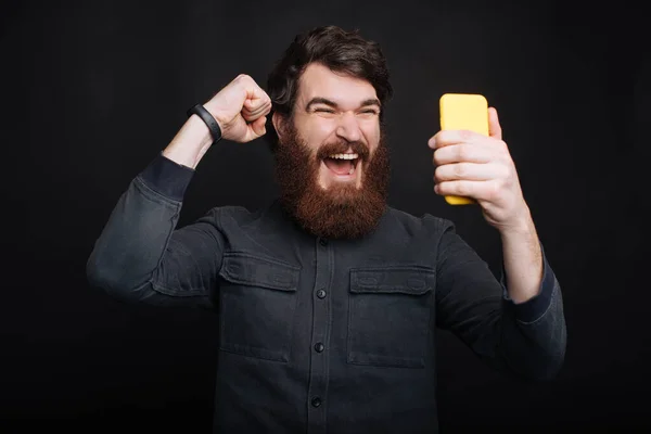 Hombre sonriente mirando el teléfono inteligente y celebrar la victoria —  Fotos de Stock