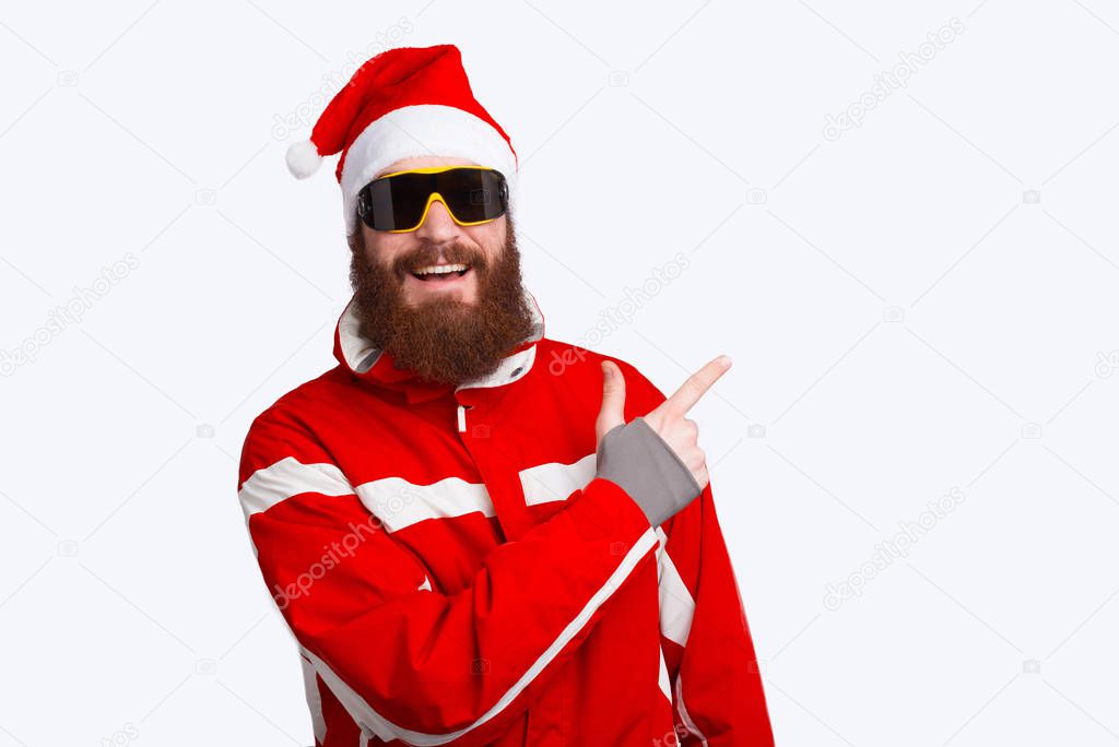 Photo of happy alpinist wearing santa claus hat and pointing away at copyspace