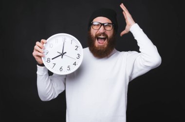 Sakallı adam çığlık atıyor ve siyah duvarda büyük bir saat tutuyor..
