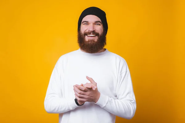 Smiling bearded young man is looking at the camera and holding his hands together near yellow wall. — 스톡 사진