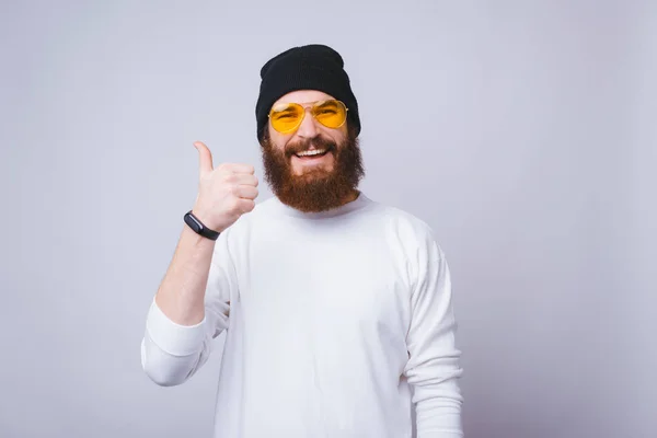 Vrolijke jongeman met baard lacht naar de camera en toont duim omhoog op witte achtergrond. — Stockfoto
