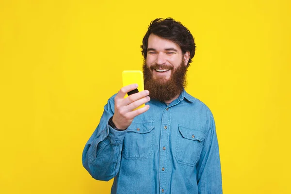 Happy man with beard using his smartphone over yellow background — Stock Photo, Image