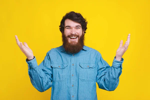 Foto di affascinante uomo hipster barbuto in camicia blu facendo gesto di benvenuto, felice di vederti — Foto Stock