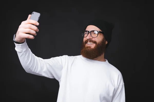 Feliz barbudo hipster hombre tomando selfie sobre fondo oscuro — Foto de Stock