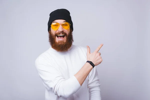 Portret modnego brodatego hipstera w żółtych okularach wskazujących na przestrzeń do kopiowania — Zdjęcie stockowe
