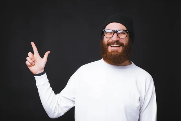 Alegre hipster hombre apuntando al copyspace sobre fondo oscuro — Foto de Stock