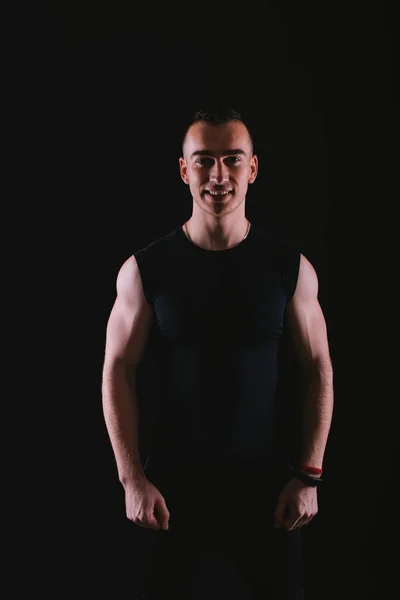 Portrait of happy young fitness trainer standing over dark background in studio — 스톡 사진