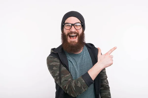 Young man with beard and eyeglasses pointing away — Stockfoto