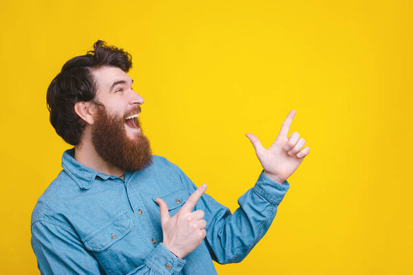 Photo of amazed man pointing away at copyspace over yellow background