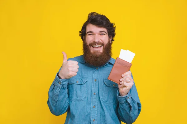 Glücklicher junger bärtiger Mann zeigt Daumen hoch und hält Pass mit Blanko-Tickets in der Hand — Stockfoto