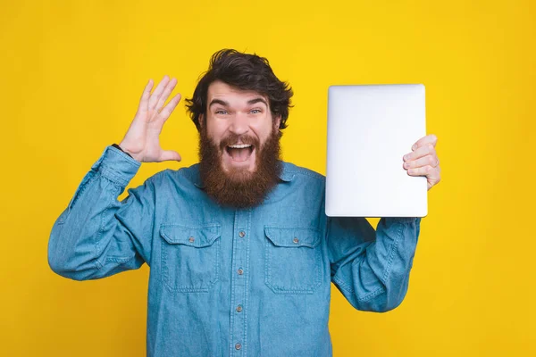 Foto de un hispano barbudo sosteniendo un nuevo portátil sobre fondo amarillo — Foto de Stock