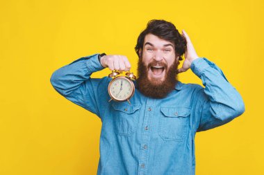 Mavi gömlekli, elinde çalar saat tutan sakallı adamın portresi.