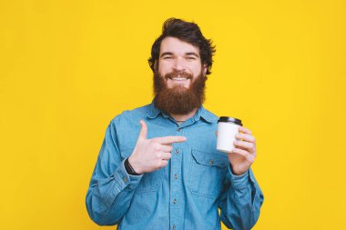 Kameraya bakıp bir fincan kahveyi işaret eden mutlu adam.