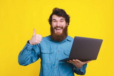 Sırıtkan sakallı mutlu bir adam kucağında dizüstü bilgisayarla