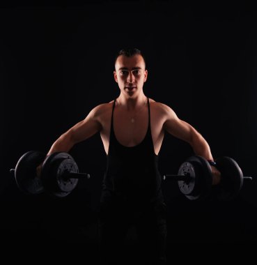 Koyu renk sırtında dambıllarla çalışan mutlu fitness adamı fotoğrafı.