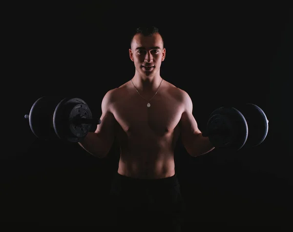 Photo of happy fitness man working with dumbbells over dark back — 스톡 사진