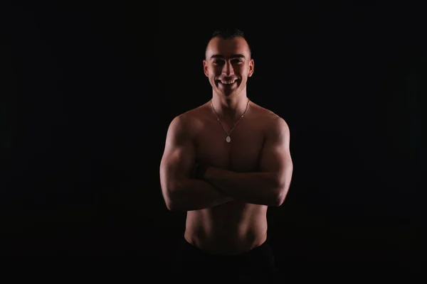 Porträt eines lächelnden muskulösen Mannes mit verschränkten Armen über dunklem Bac — Stockfoto