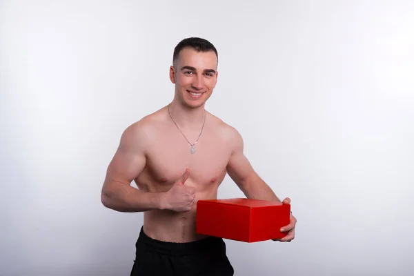 Giovane uomo in forma che tiene la scatola e mostra i pollici in alto — Foto Stock
