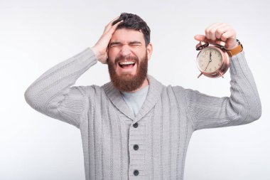 Genç adam beyaz arka planda bir saat tutarken baş ağrısı çekiyor..