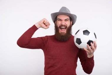 Genç sakallı adam bağırıyor ve elinde futbol topu tutuyor..