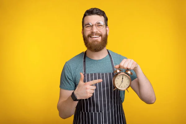 Фото улыбающегося молодого шеф-повара в форме, указывающего на будильник, время приготовления — стоковое фото