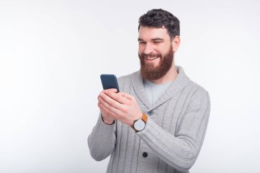 Mutlu sakallı adam beyaz arka planda koyu mavi telefonuna bir şeyler yazıyor..