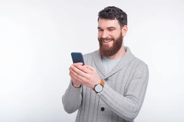Happy bearded man is typing something on his dark blue phone on white background. — Stock Photo, Image