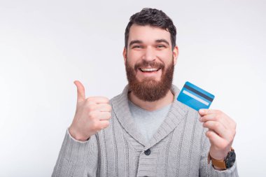 Kredi kartım olması benim en iyi dileğim. Mutlu genç sakallı öğrenci ve bir adam elinde mavi bir kart tutuyor ve jest yapıyor..