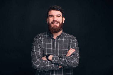Yakışıklı sakallı adam karanlık arka planda duruyor, kolları bağlı..