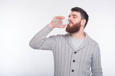 Yakışıklı adam beyaz arka planda bir şişeden su içiyor..