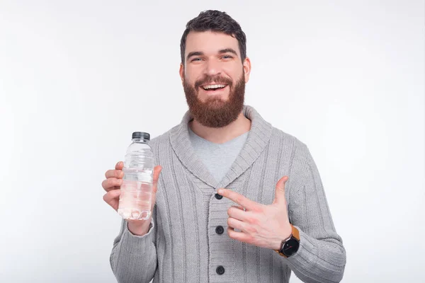 Не забудьте гідратувати. Щасливий молодий бородатий чоловік тримає пляшку води і вказує на неї . — стокове фото