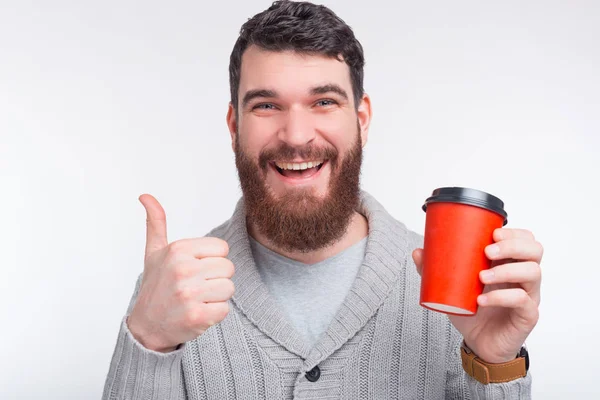 I like this coffee or tea. Happy bearded man is holding a red paper cup shows like gesture.