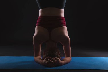 Güzel bir genç kadın, siyah arka planda bir stüdyoda çalışıyor. Mavi minder üzerinde yoga egzersizi yapıyor. Desteklenen amuda salamba sirsasana çeşitleri..