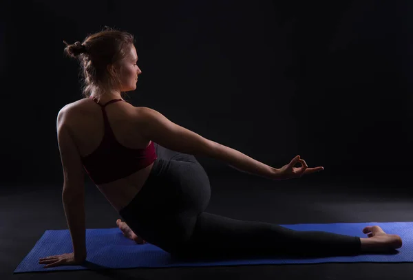 Joven mujer atractiva practicando yoga, sobre fondo negro, y haciendo algunos ejercicios de estiramiento . —  Fotos de Stock