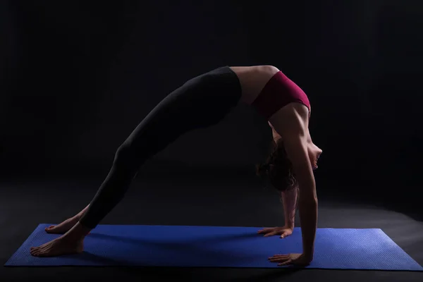 Молода жінка балансує в сетуасані або робить вправи на йозі в Bridge Pose в студії на чорному тлі. — стокове фото