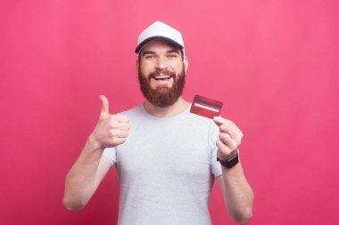 excited man with beard in t-shirt showing thumbs up and holding credit card