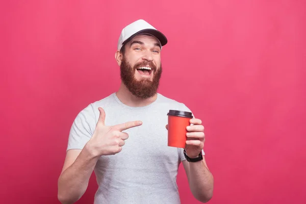 Foto eines fröhlichen Mannes mit Bart, der auf eine Tasse Kaffee to go zeigt — Stockfoto
