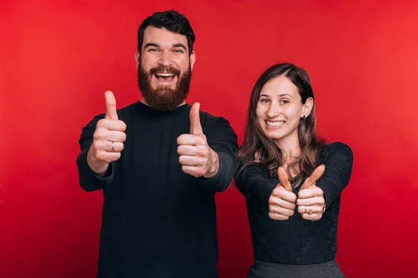 Foto de jovem casal alegre em pé sobre fundo vermelho e mostrando os polegares para cima — Fotografia de Stock