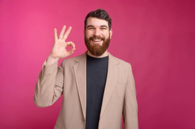 Ceket giyen neşeli sakallı adam iyi bir jest yapıyor.