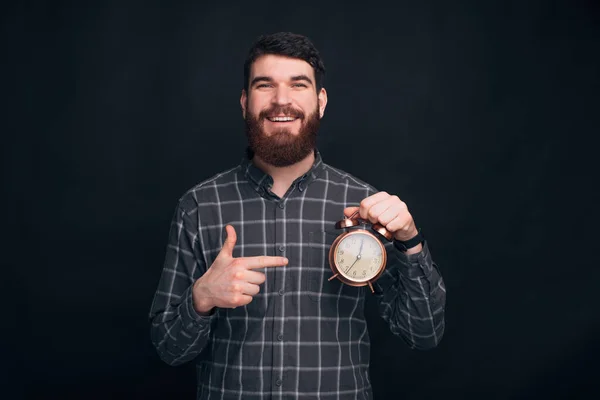 Lächelnder bärtiger Mann zeigt auf einen Wecker — Stockfoto