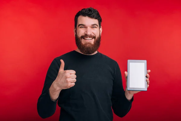 Un homme souriant montre le pouce levé et l'écran vide d'une tablette sur — Photo