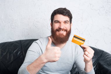 Mutlu adam başparmak gösteriyor ve kredi kartı tutuyor. 