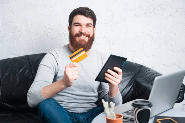 Hombre alegre sonriendo y usando tarjeta de crédito y tableta — Foto de Stock