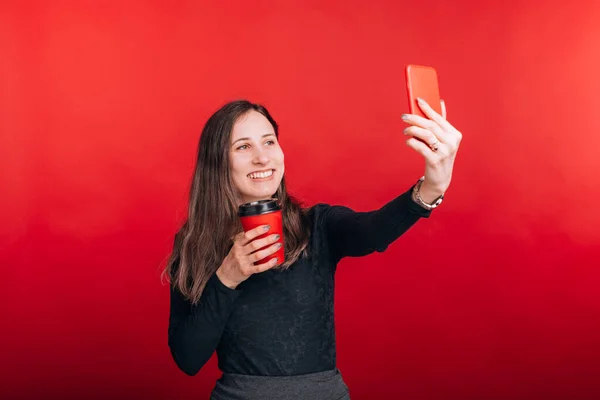 Neşeli genç bayan elinde kırmızı bir kağıt bardakla selfie çekiyor. — Stok fotoğraf