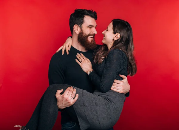 Homem barbudo feliz si segurando sua mulher no fundo vermelho. Casal alegre está desfrutando cada vez mais — Fotografia de Stock