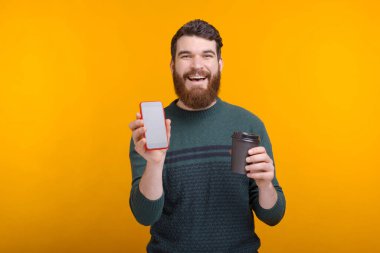 Kahveni internetten sipariş et. Heyecanlı adam elinde kahve fincanı ve sarı arka planda boş bir ekran telefonu tutuyor.