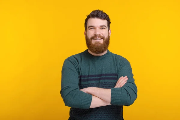 Un homme barbu souriant avec les bras croisés regarde la caméra sur fond jaune — Photo