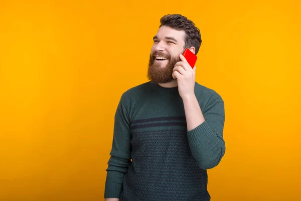 Cheerful bearded man is talking on the phone and smiling on yellow background — Stock Photo, Image