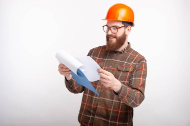 Başlık takan genç mühendis beyaz arka plandaki kağıtlara bakıyor.